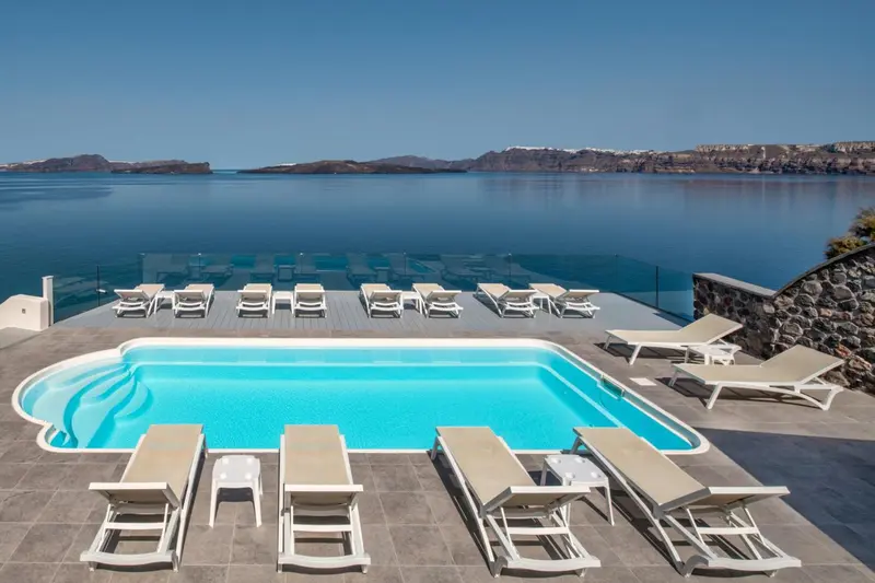 Une piscine rectangulaire bordée de transats offre une vue sur la mer et les collines environnantes.