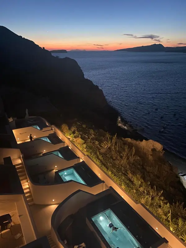 Vue panoramique sur la mer au coucher du soleil depuis une terrasse avec piscines.