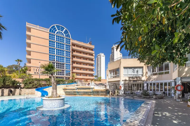 Vue d'un bâtiment beige avec des fenêtres bleues et une piscine au premier plan.