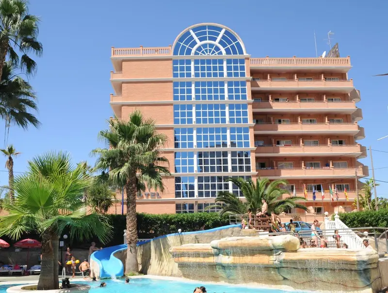 Bâtiment de plusieurs étages avec des palmiers et une piscine au premier plan.