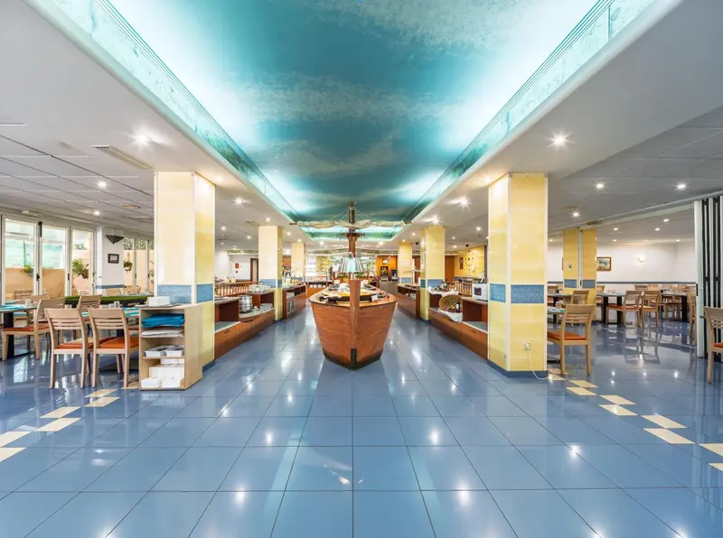 Une salle lumineuse avec des tables et des chaises disposées de part et d'autre d'un élément décoratif en forme de bateau.