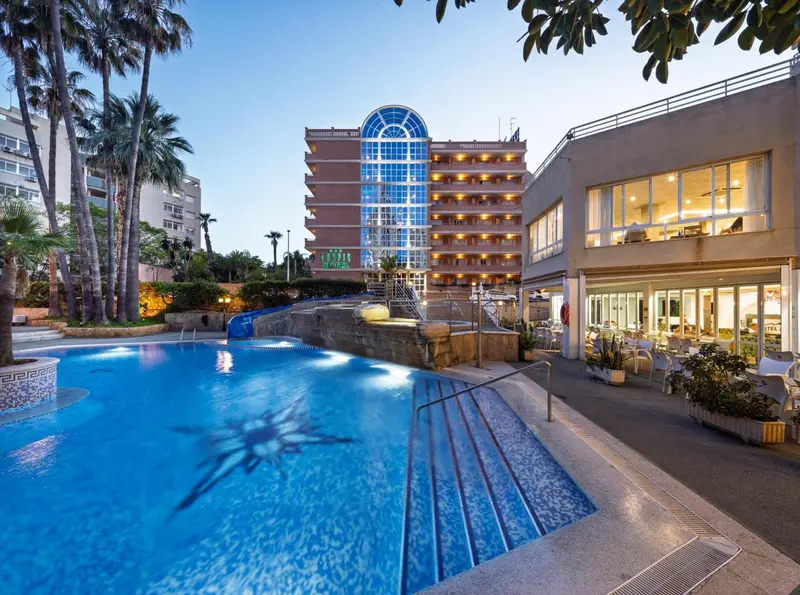 Une piscine bleue au premier plan, avec un bâtiment illuminé en arrière-plan.