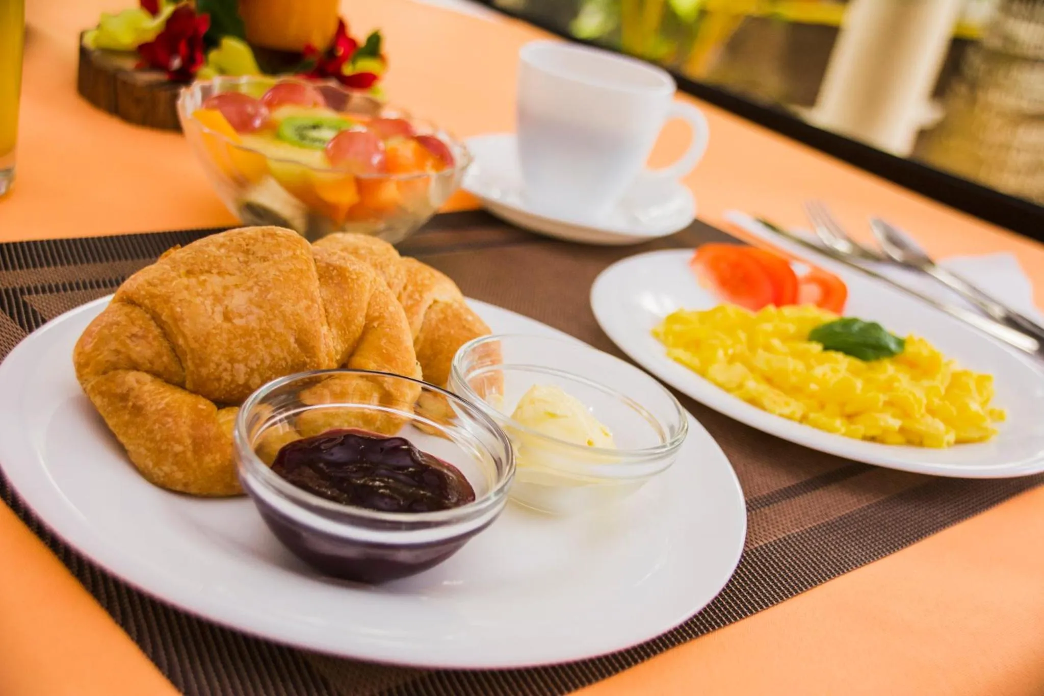 Une table est dressée avec un petit-déjeuner composé de viennoiseries, de fruits et d'oeufs brouillés.