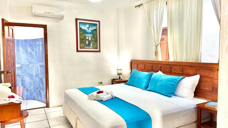 Une chambre lumineuse avec un grand lit recouvert d'une courtepointe turquoise et de coussins.
