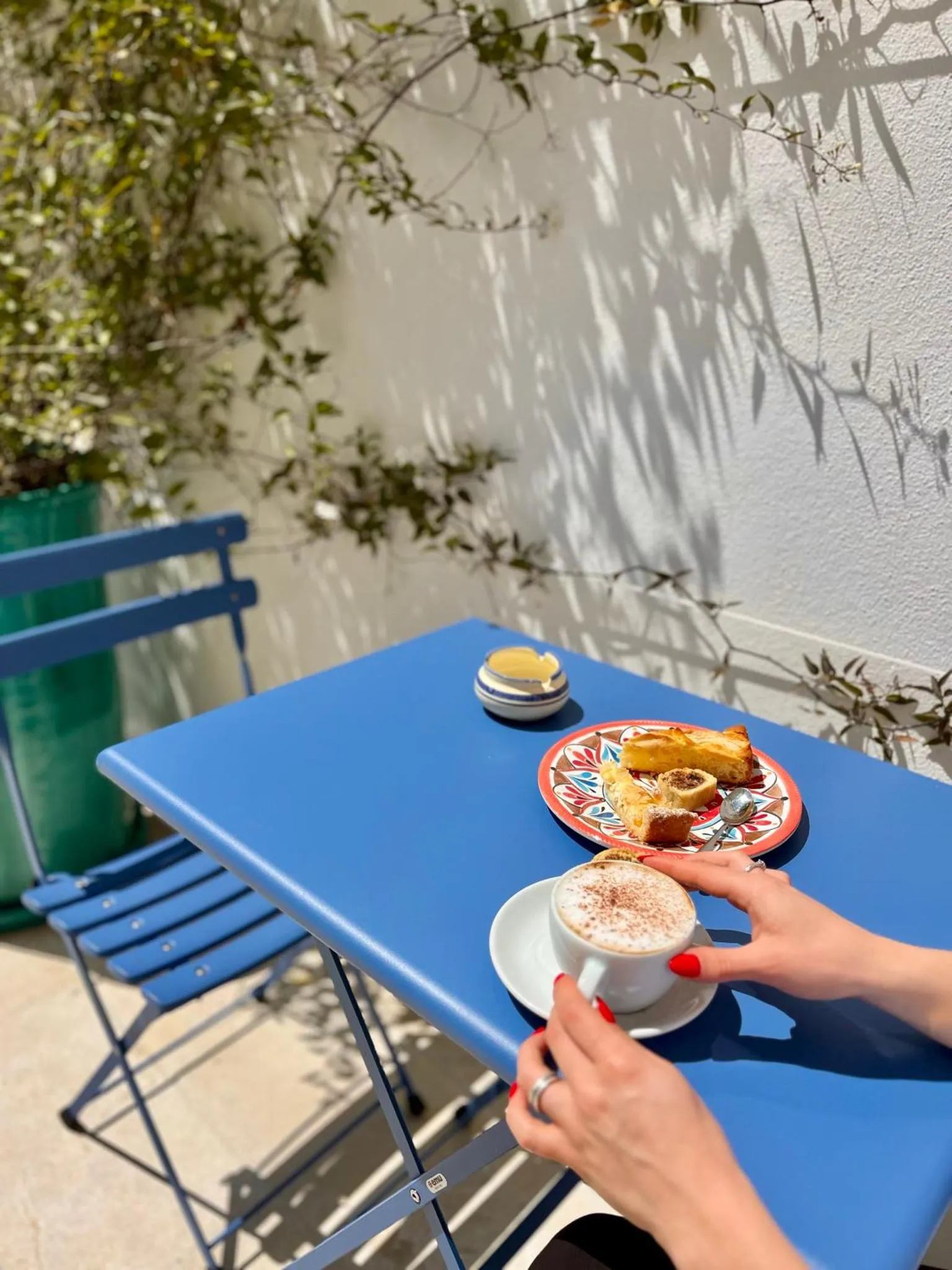 Une table bleue avec une boisson chaude et une pâtisserie sur une terrasse ensoleillée.
