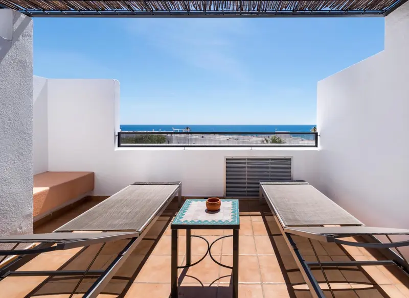 Terrasse carrelée avec transats et table basse donnant sur la mer.