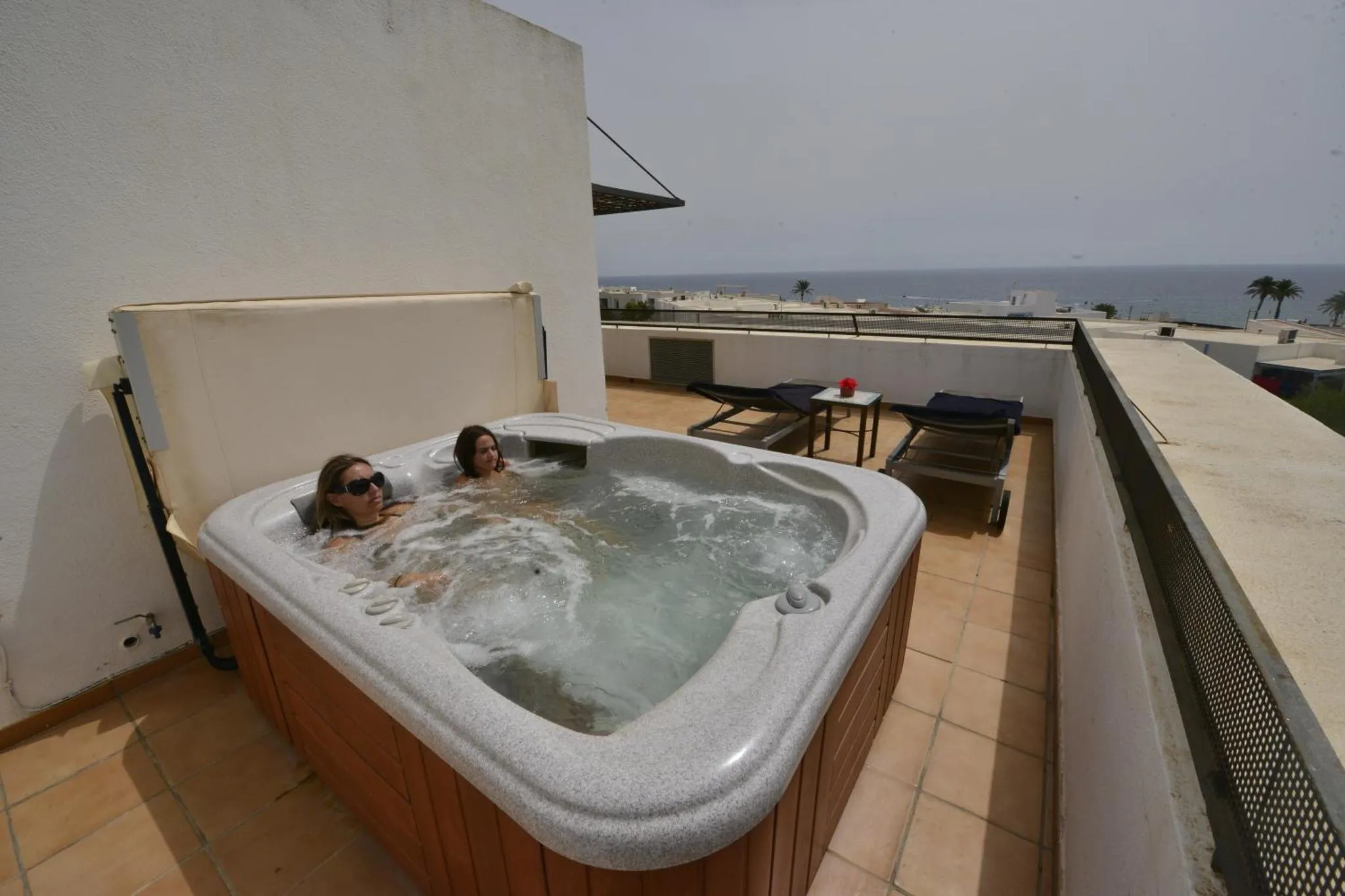 Une personne se détend dans un jacuzzi sur une terrasse avec vue sur la mer.