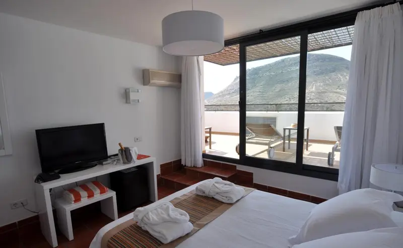 Une chambre lumineuse s'ouvre sur une terrasse avec vue sur les montagnes.