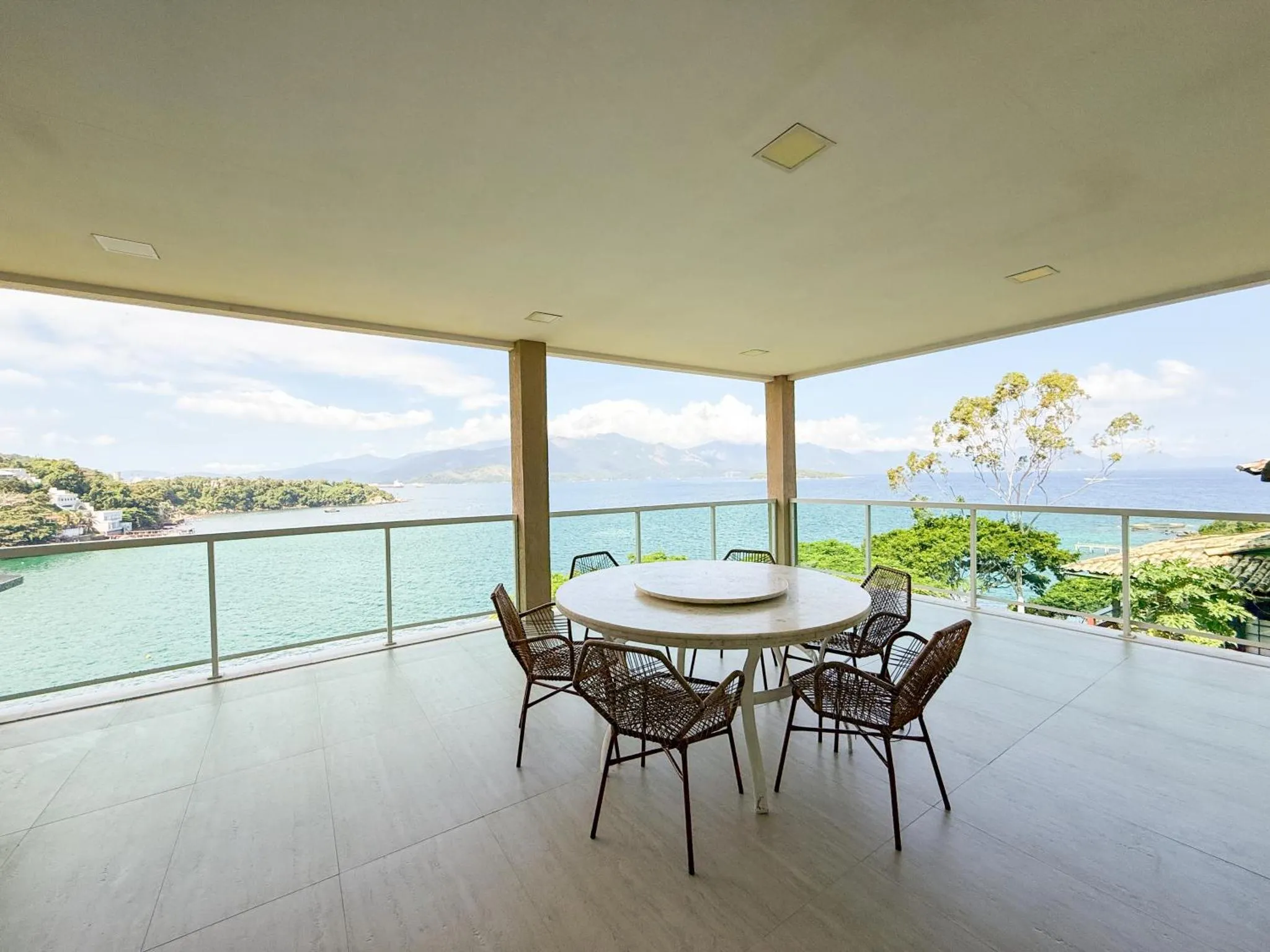 Une table ronde et des chaises se trouvent sur une terrasse carrelée avec vue sur la mer et la végétation.