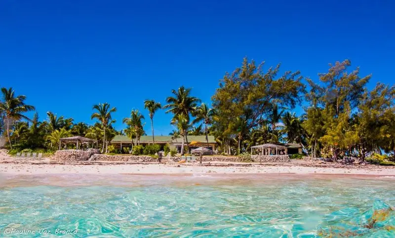 Plage de sable blanc bordée de végétation tropicale et d'habitations.