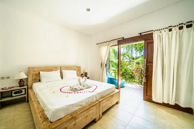 Une chambre lumineuse avec un lit décoré de fleurs et une porte ouverte sur un jardin.
