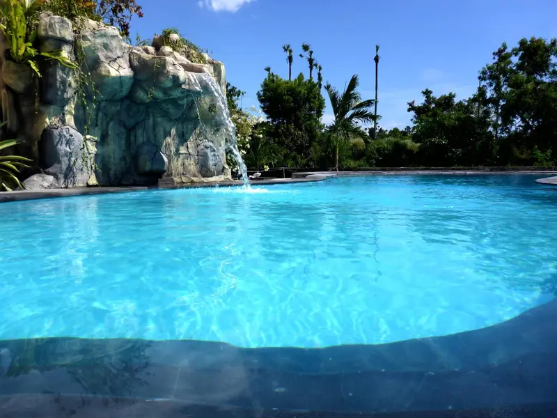 Une piscine turquoise bordée de rochers et de végétation luxuriante sous un ciel bleu.