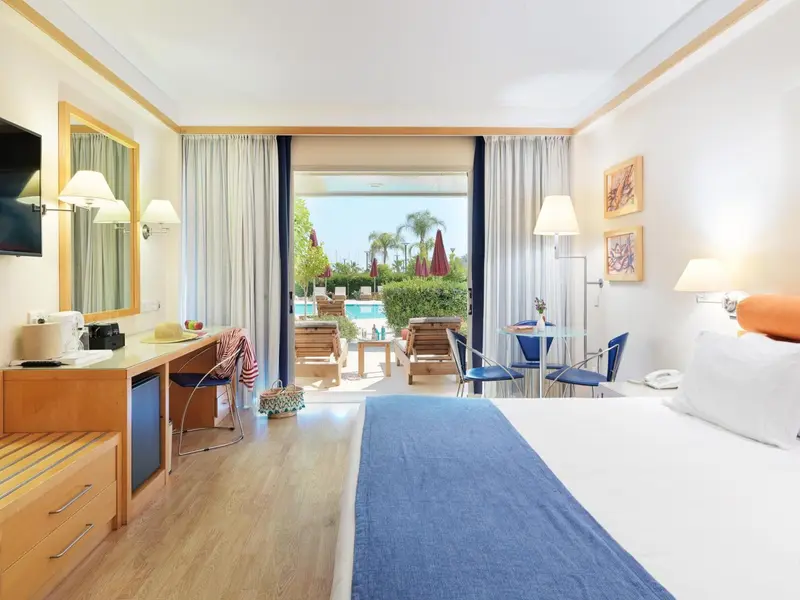 Chambre lumineuse avec un lit et un accès à une terrasse avec vue sur une piscine.