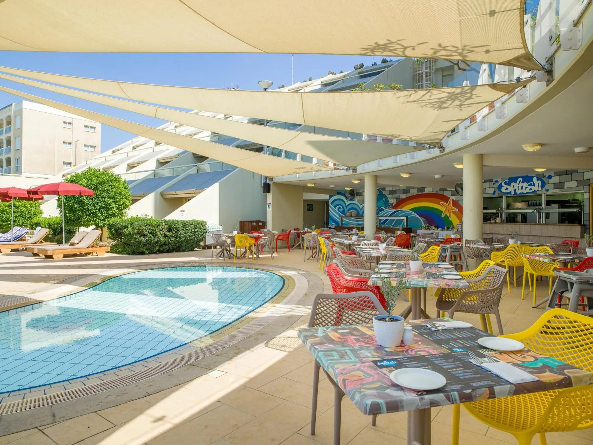 Terrasse ombragée avec tables et chaises près d'une piscine.
