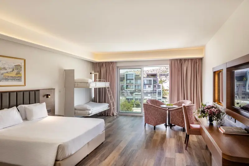 Chambre lumineuse avec un lit double et un lit superposé, un coin salon et une vue sur l'extérieur.