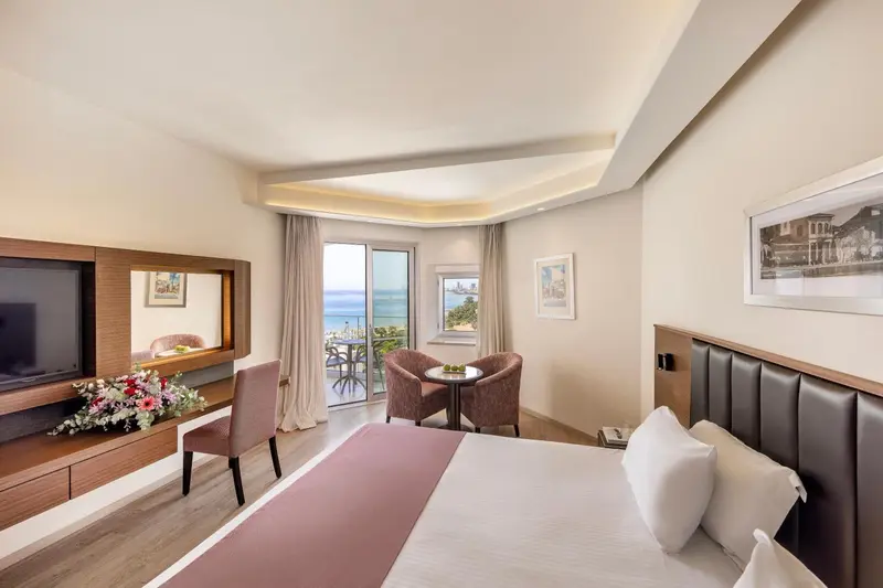 Une chambre lumineuse avec un lit double et un coin salon donnant sur une vue mer.