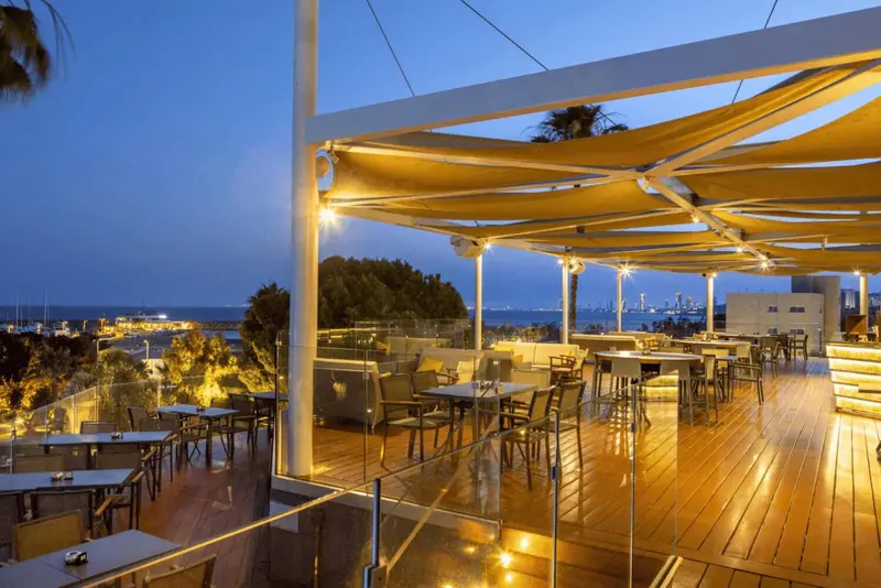 Terrasse lumineuse avec tables et chaises donnant sur la mer au crépuscule.