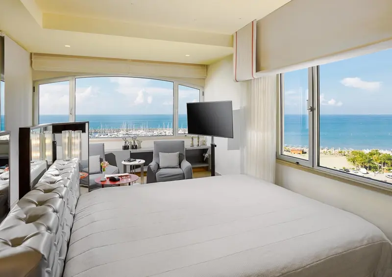 Chambre lumineuse avec un grand lit donnant sur une vue mer et un coin salon.
