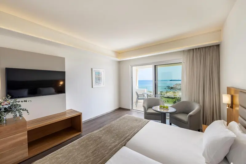 Chambre lumineuse avec un lit confortable et un accès à un balcon offrant une vue sur la mer.