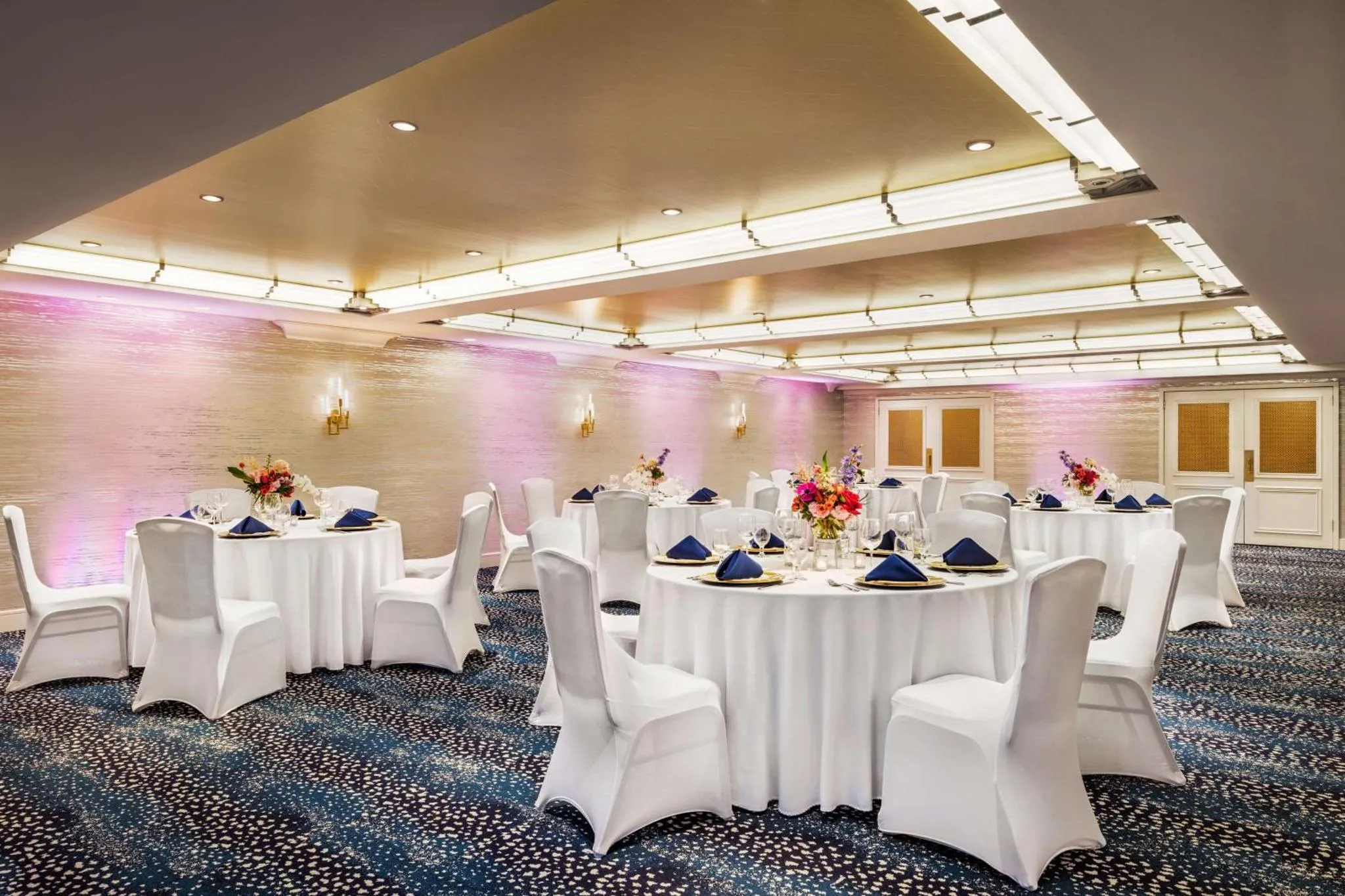 Une salle lumineuse est aménagée avec des tables rondes nappées et des chaises habillées.