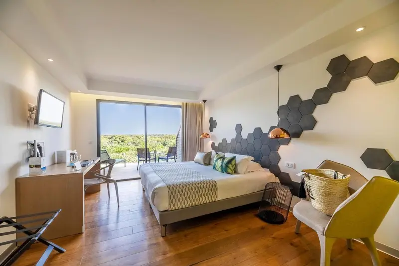Chambre lumineuse avec un grand lit et une vue sur la végétation.