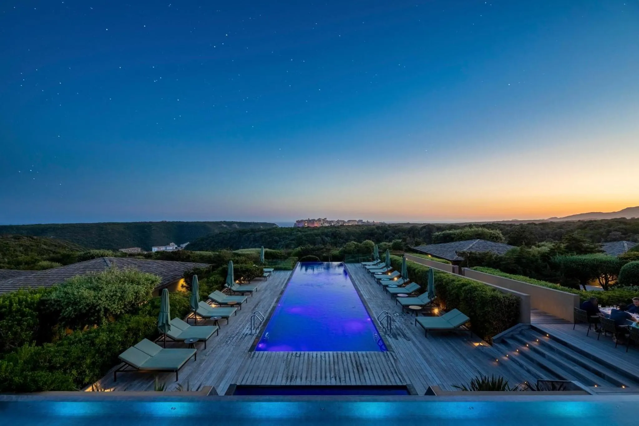 Une piscine rectangulaire illuminée au crépuscule, avec des transats alignés sur le bord.
