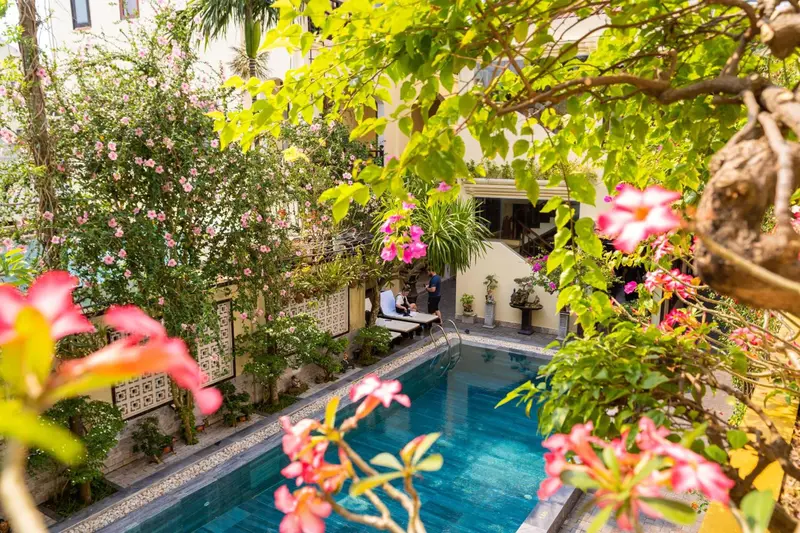 Une piscine rectangulaire entourée de végétation luxuriante et de fleurs colorées.