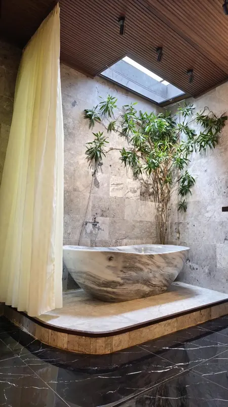 Une baignoire blanche surélevée se trouve dans une salle de bain moderne avec une douche à l'italienne et une végétation luxuriante.