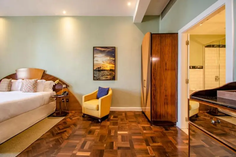 Une chambre lumineuse avec un lit, un fauteuil et un accès à une salle de bain.