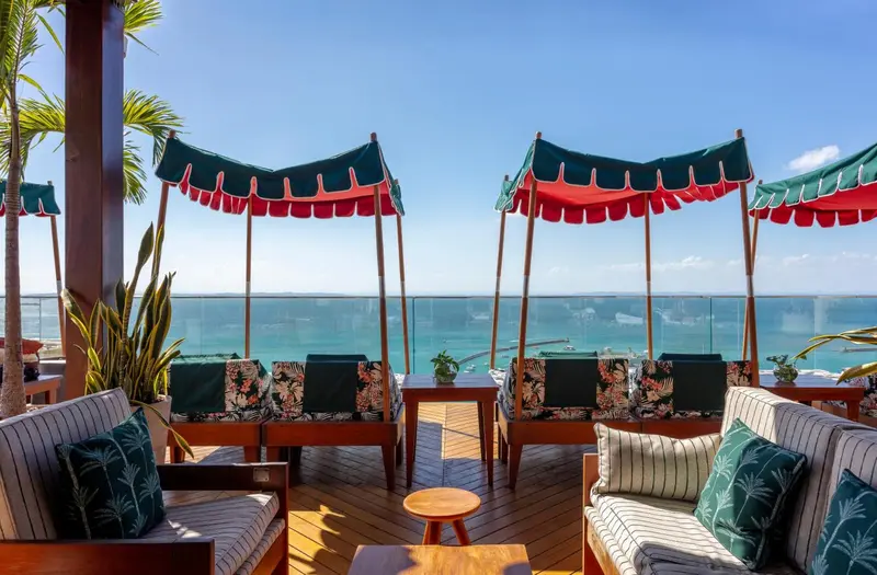 Terrasse ombragée avec mobilier de salon et vue sur la mer.