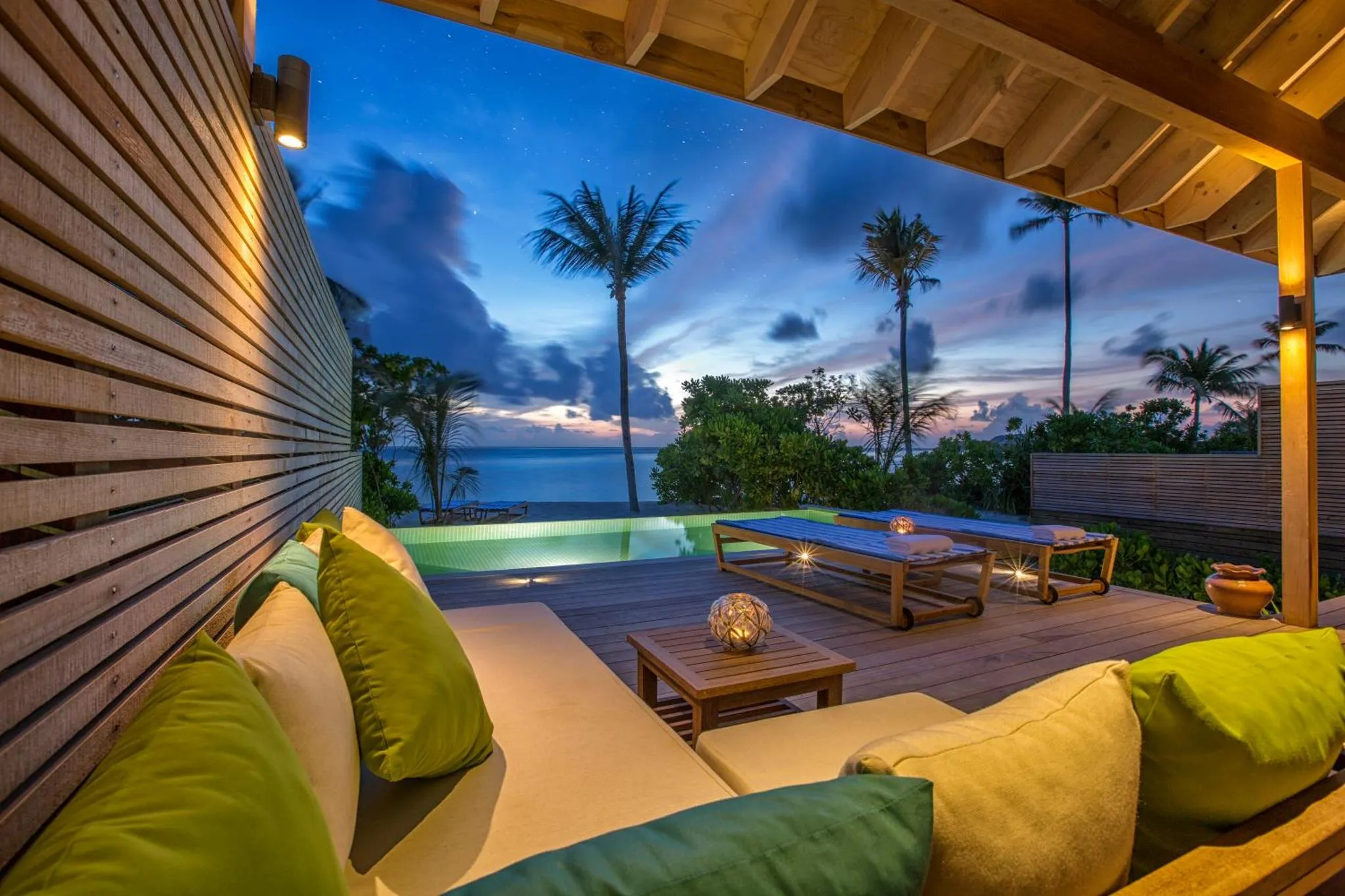 Terrasse aménagée avec salon et piscine donnant sur la mer au crépuscule.