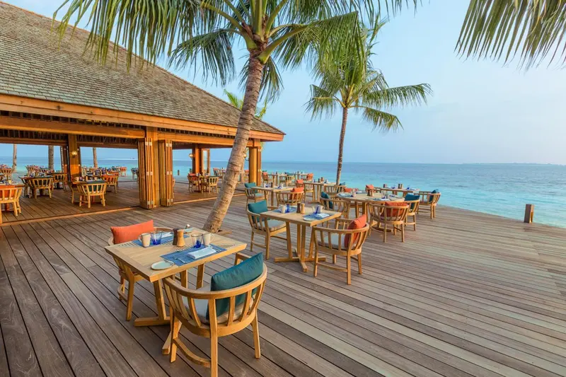 Terrasse en bois avec tables et chaises face à la mer.