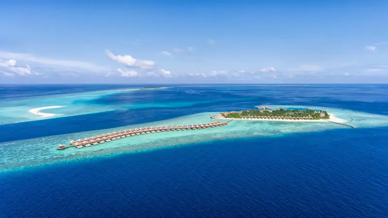 Vue aérienne d'une île tropicale avec des bungalows sur pilotis et une eau turquoise.