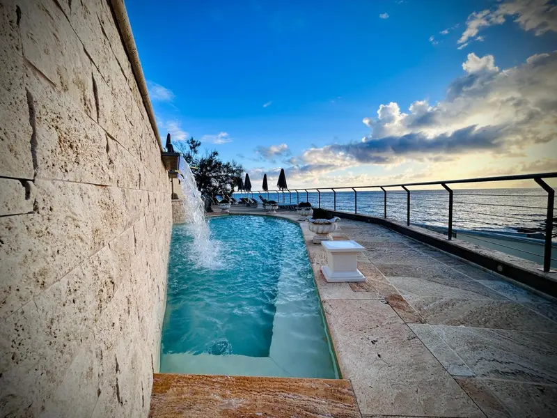 Une piscine rectangulaire avec une cascade artificielle surplombe la mer.