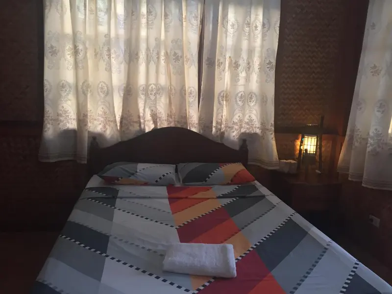 Une chambre avec un lit recouvert d'une courtepointe colorée et des rideaux blancs.