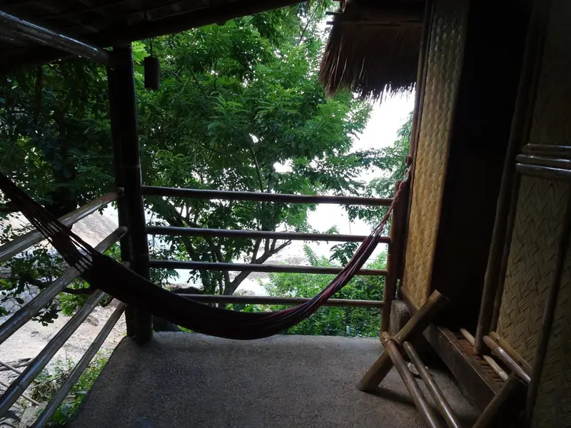 Un hamac est suspendu sur une terrasse ombragée avec vue sur la végétation.