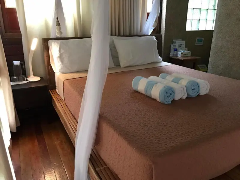 Une chambre avec un grand lit recouvert d'une moustiquaire et de serviettes enroulées.