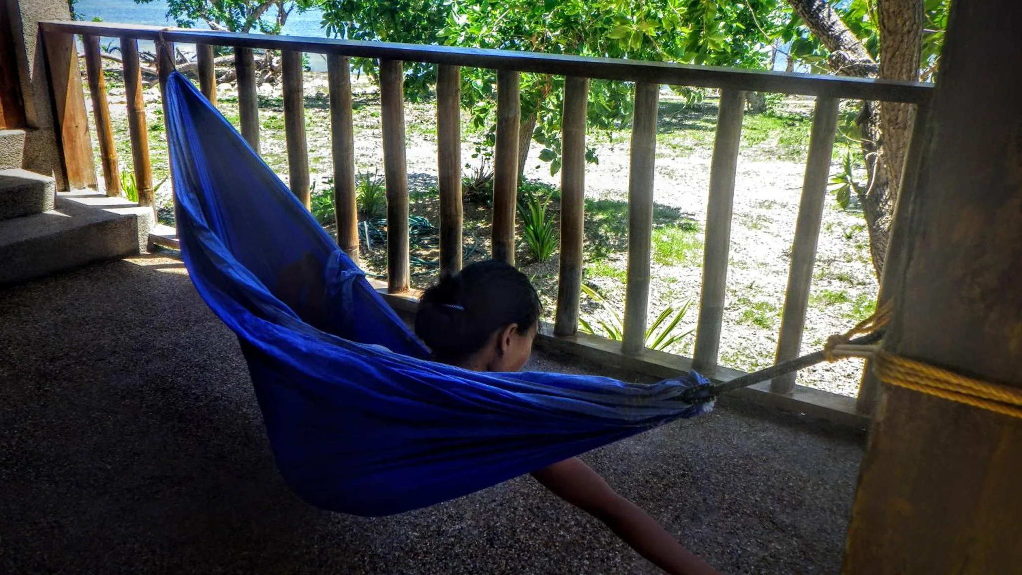 Une personne se détend dans un hamac bleu sur une terrasse.