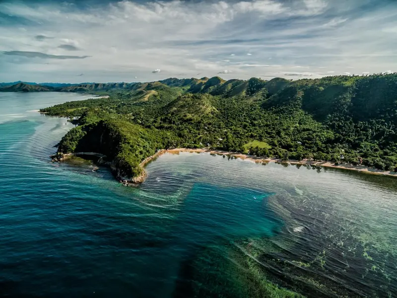 Vue aérienne d'une côte rocheuse bordée d'une plage et d'une végétation luxuriante.