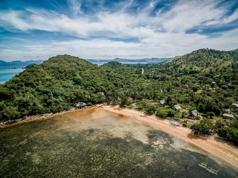 Vue aérienne d'une plage de sable fin bordée d'une eau turquoise et d'une végétation luxuriante.