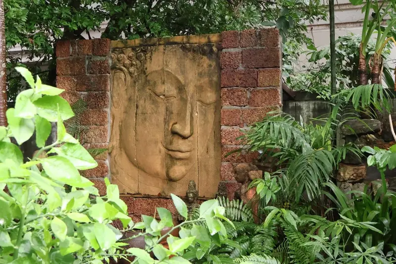 Sculpture d'un visage humain sur un mur de pierre, entourée de végétation luxuriante.