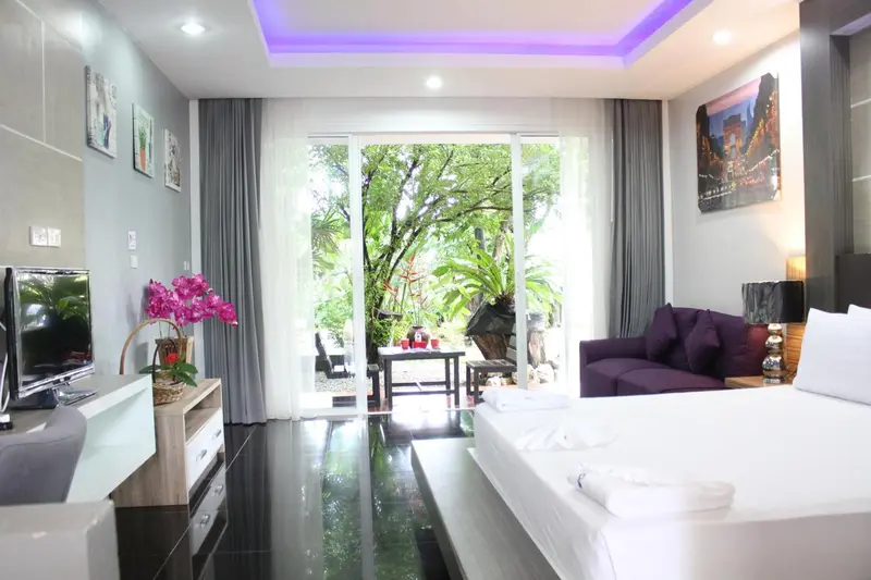 Une chambre lumineuse avec un grand lit et un canapé violet donne sur une végétation luxuriante.