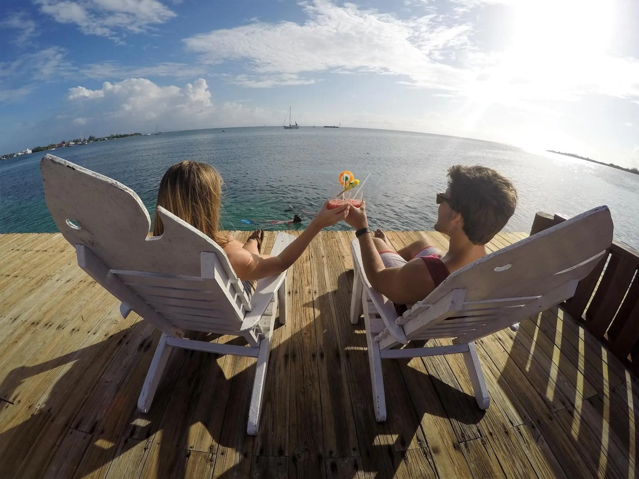 Deux personnes assises sur des chaises longues face à la mer, levant leurs verres.