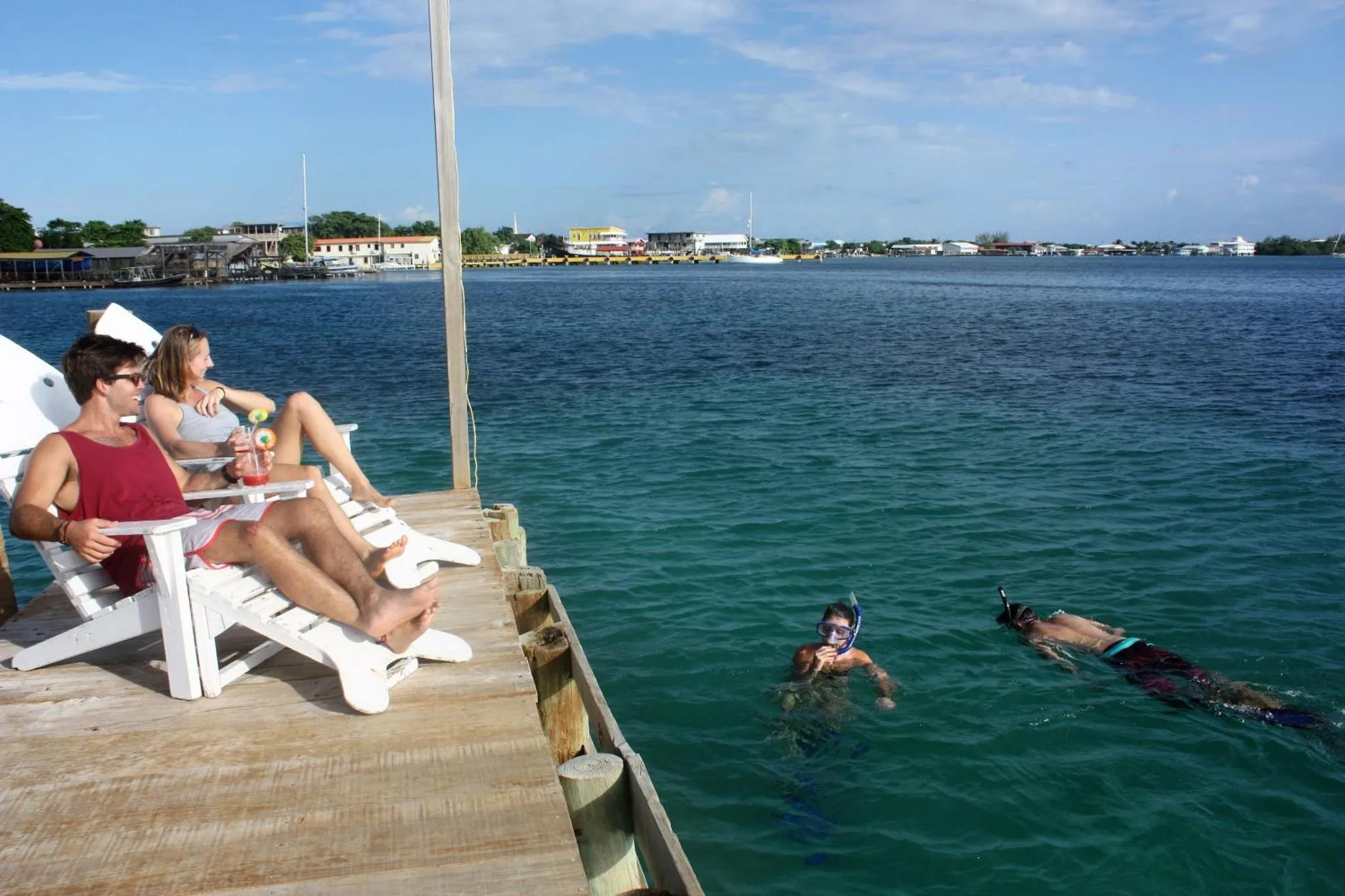 Des personnes se détendent sur un ponton en bois au-dessus de l'eau turquoise.