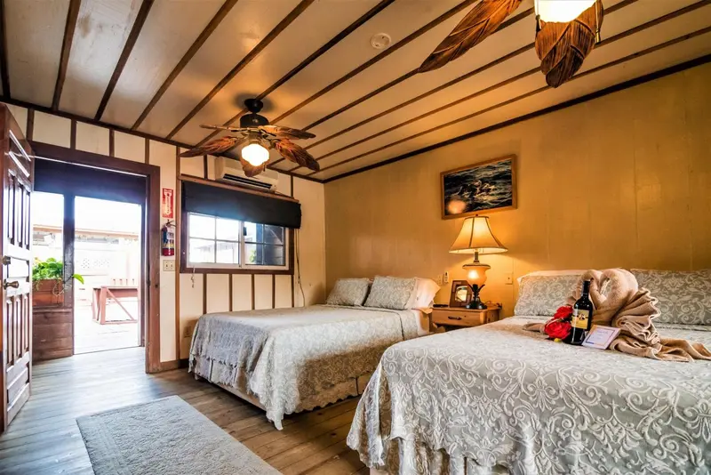 Chambre lumineuse avec deux lits et vue sur une terrasse en bois.