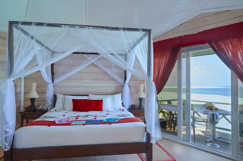 Lit à baldaquin blanc dans une chambre décorée de rouge, avec vue sur la mer.