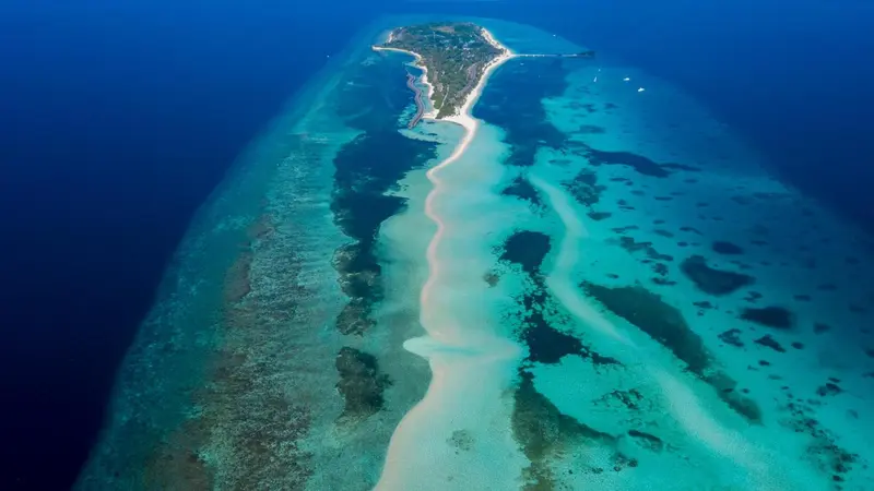 Vue aérienne d'une île tropicale entourée d'eaux turquoise et de récifs coralliens.