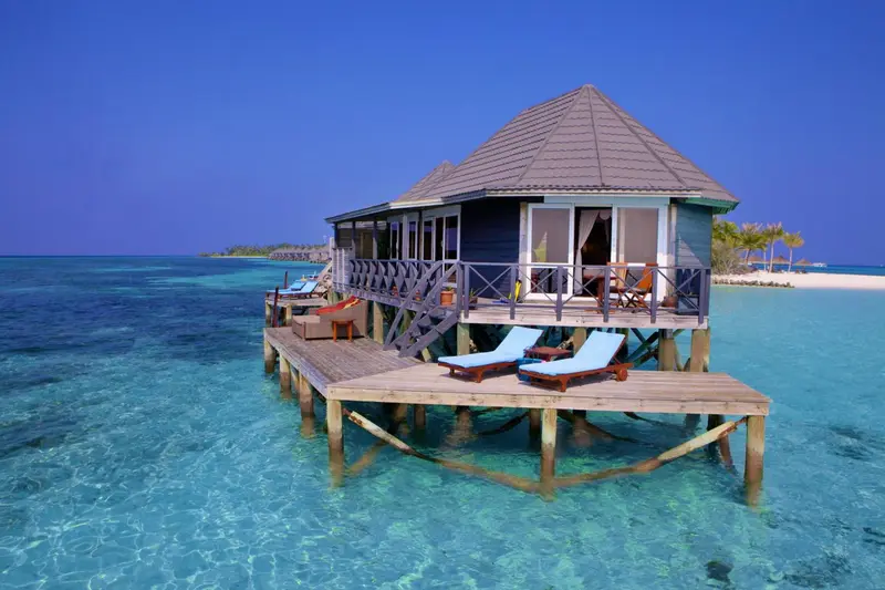 Une maison sur pilotis surplombe une eau turquoise et peu profonde.