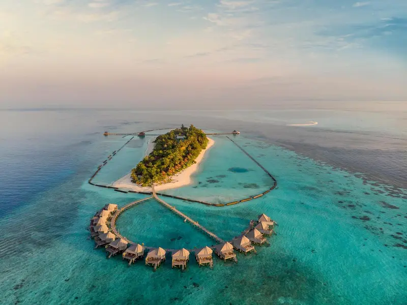 Vue aérienne d'une île tropicale avec des bungalows sur pilotis et une plage de sable blanc.