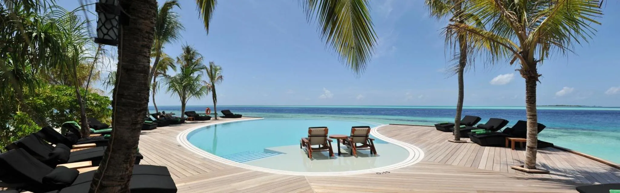 Transats et parasols bordent une piscine à débordement avec vue sur la mer.